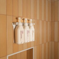Un baño con dispensador mural que contiene tres botellas de jabón de manos y cuerpo O&M.
