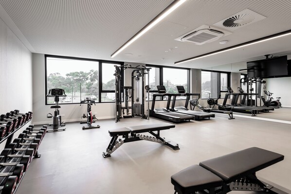 A gym with exercise equipment, large windows, and a bench. - Hotel Panorama (Panorama)