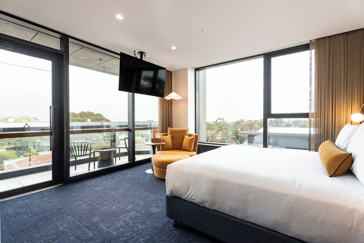 A hotel room with a large bed, a TV, a chair, and a balcony with a view.