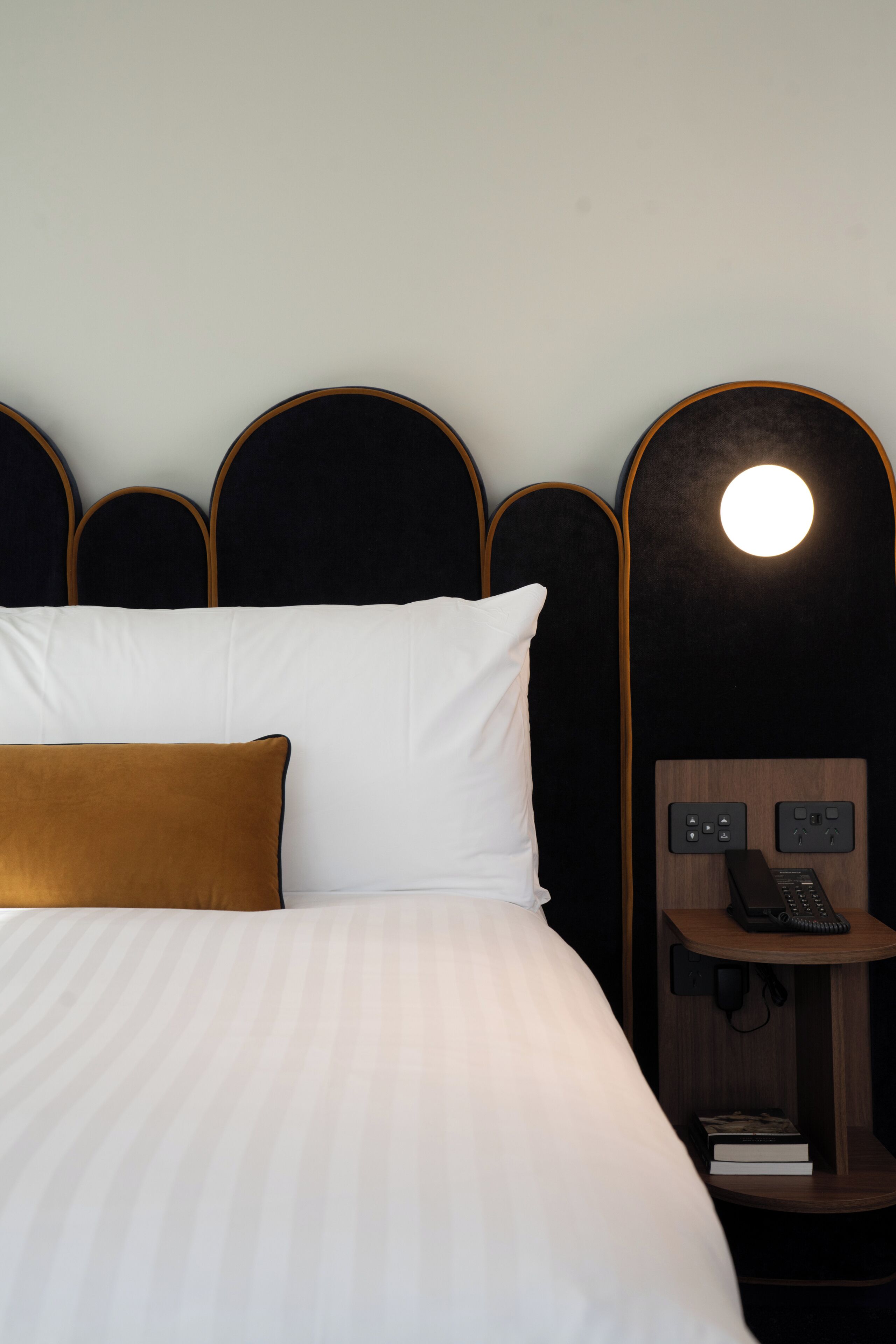 A hotel room with a bed, a bedside table with a phone, and a wall-mounted light.