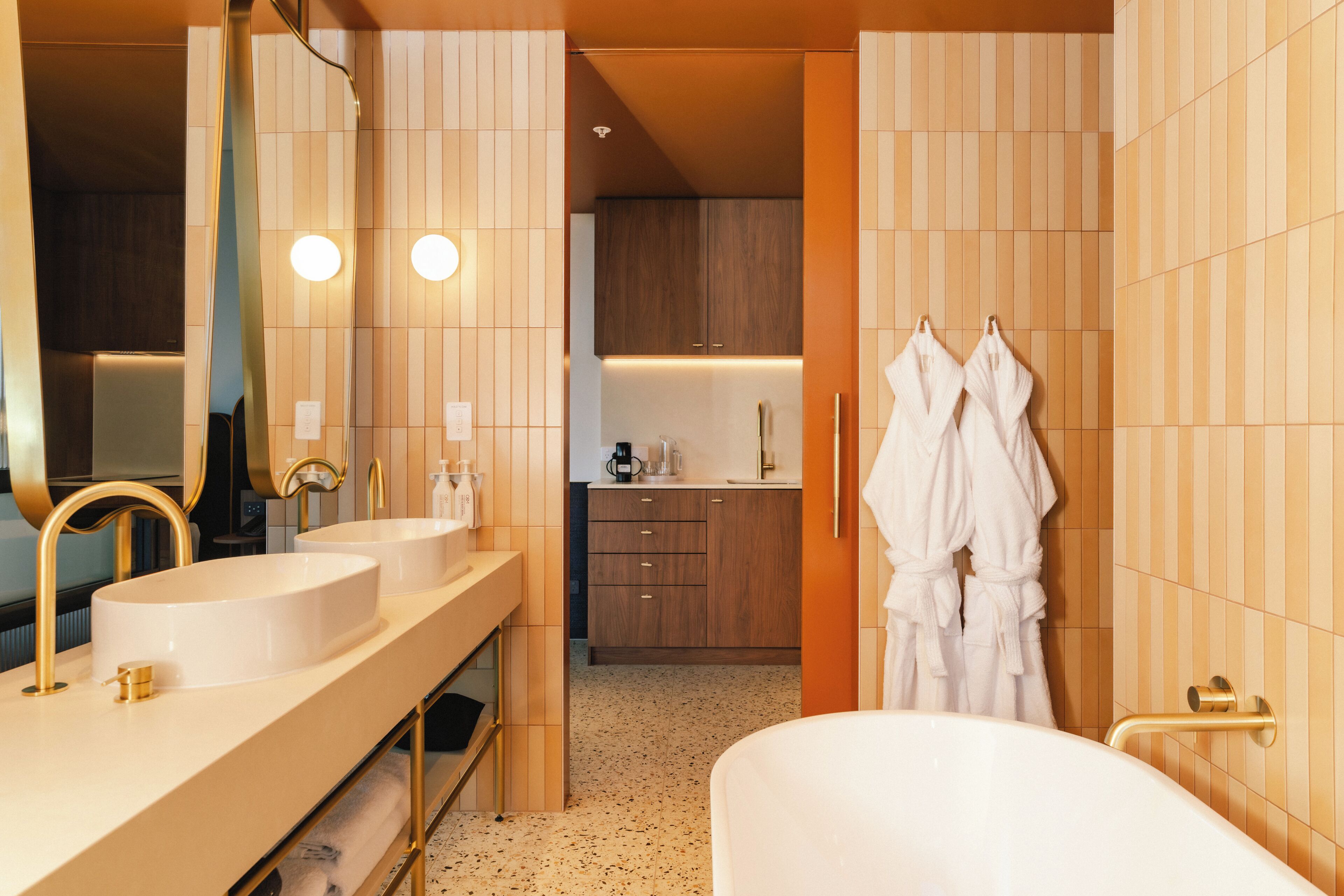 A modern bathroom with dual sinks, a large mirror, a bathtub, and wooden cabinetry.