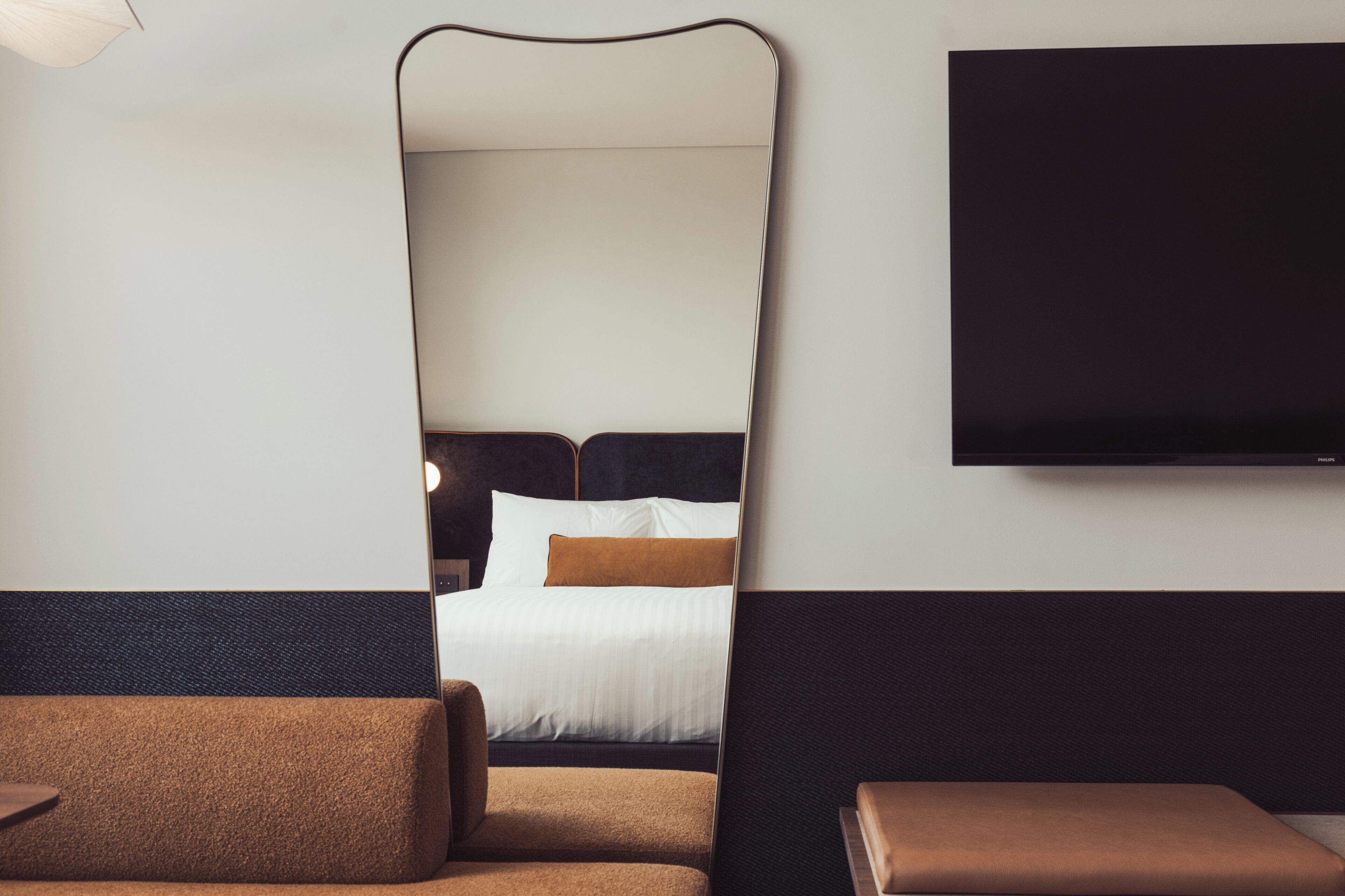 Ein modernes Hotelzimmer mit einem großen Bett, einem flachbildfernseher an der Wand und einer Sitzecke mit Sofa und Hocker.