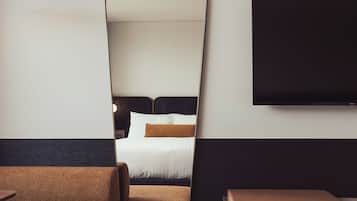 Ein modernes Hotelzimmer mit einem großen Bett, einem flachbildfernseher an der Wand und einer Sitzecke mit Sofa und Hocker.