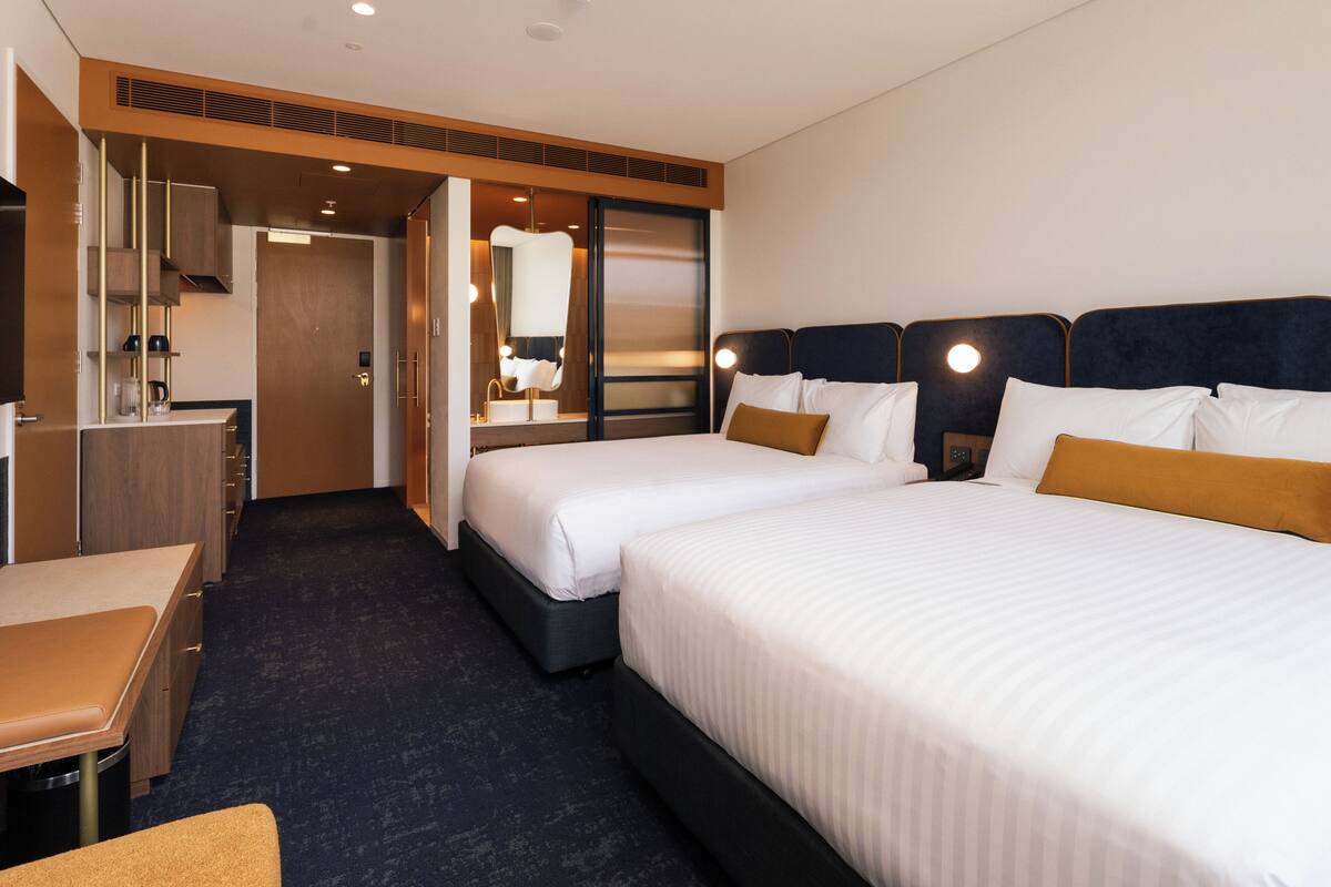 A hotel room with two beds, a desk, and a mirror.