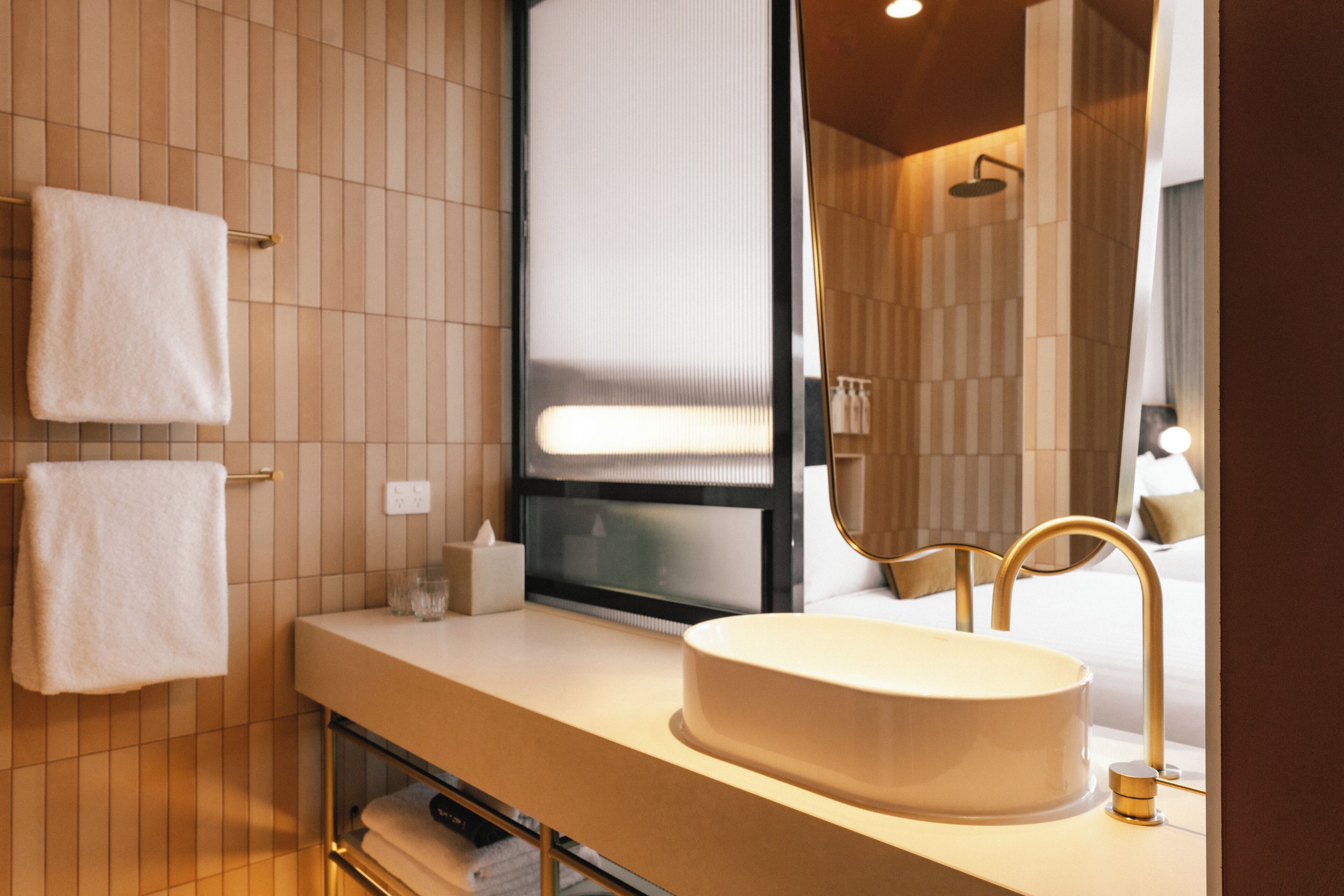 Un baño moderno con un espejo grande, un lavabo redondo y dos toallas colgadas en un perchero.