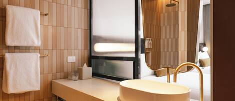Un baño moderno con un espejo grande, un lavabo redondo y dos toallas colgadas en un perchero.