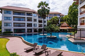 A resort with a swimming pool, lounge chairs, and a multi-story building with balconies.