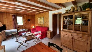 Interior acogedor de una cabaña de madera con un sofá rojo, una mesa de comedor y un aparador con puertas de cristal.