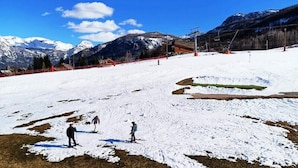 Pista de esquí nevada con esquiadores, un telesilla y montañas al fondo.
