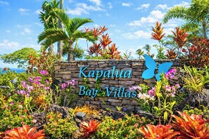 Ein Steinschild mit der Aufschrift 'Kapalua Bay Villas', umgeben von tropischen Pflanzen und Palmen.