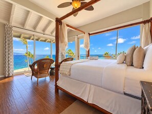 A four-poster bed with a view of the ocean, a wicker chair, and a ceiling fan. - Kapalua Bay | Ocean View 2 BR, Sleeps 8 | Car Incl. w/ 6+ Nights | KBV ML-1966 by KBM (Lahaina)