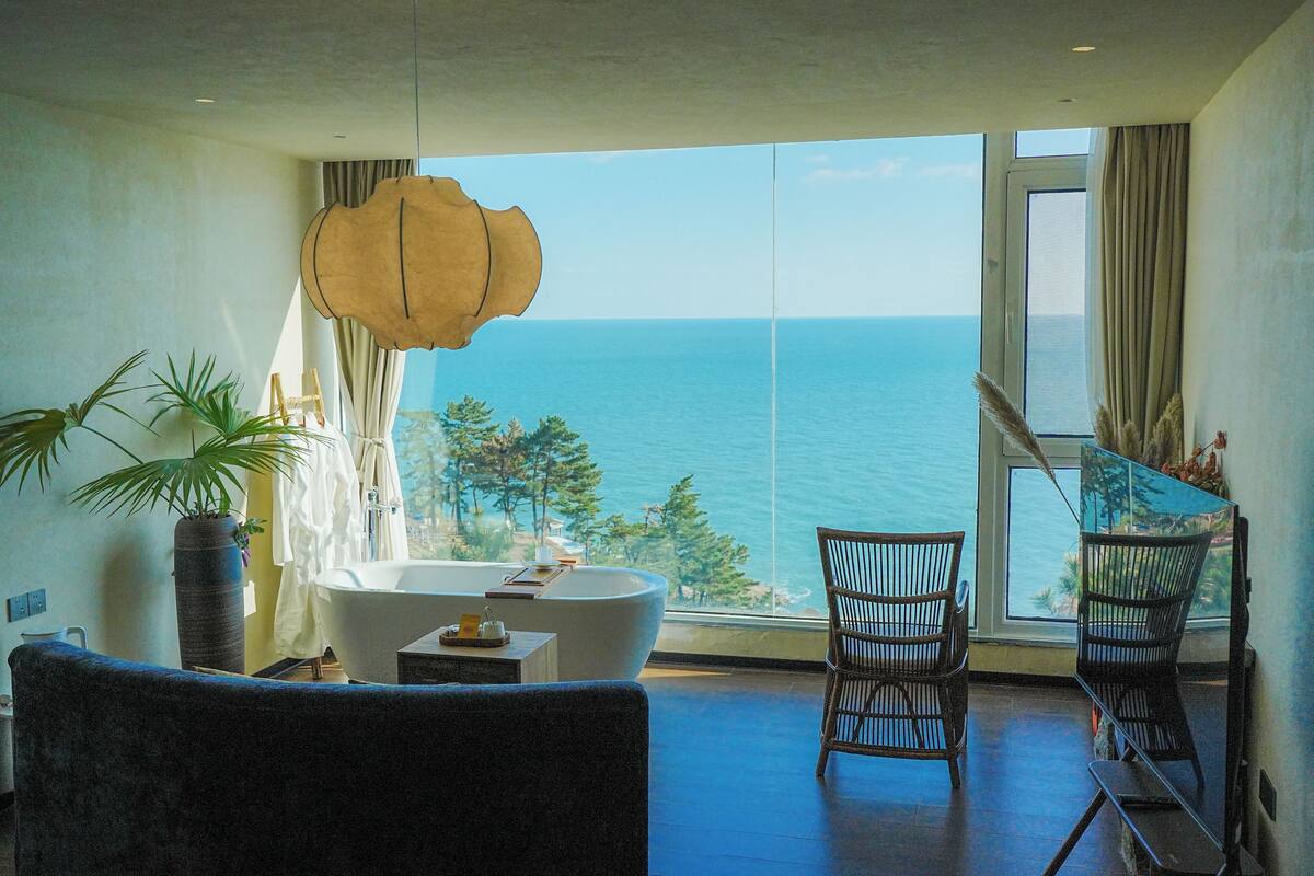 Un baño moderno con bañera, una planta grande en maceta y vistas al mar.