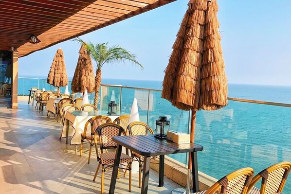 A seaside terrace with tables and chairs, thatched umbrellas, and a view of the ocean. - Qingdao Momer Cliff Ocean View Villas (Qingdao)