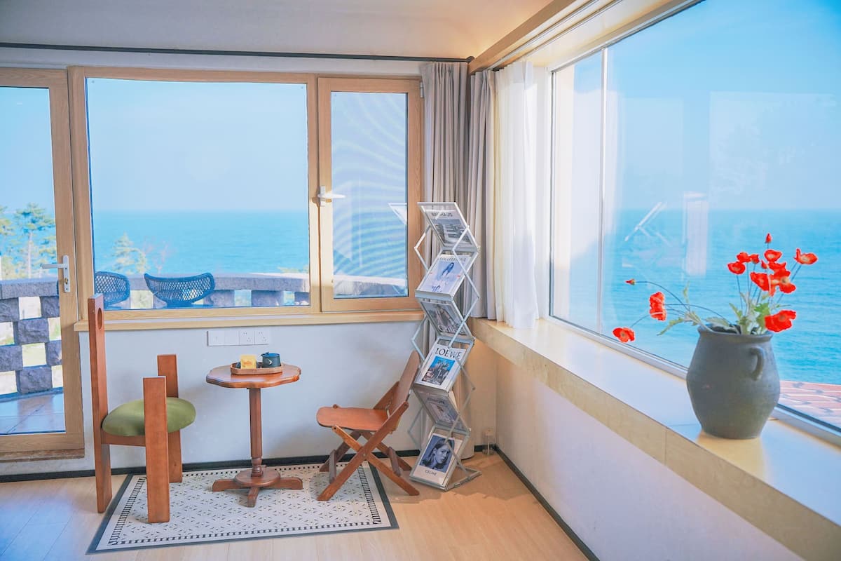 Una habitación con vista al mar, una silla de madera, una mesita y un atril para folletos.
