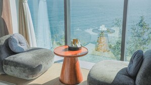 Ein modernes Zimmer mit großem Fenster mit Blick auf ein Gewässer, einem runden Holztisch und zwei grau gepolsterten Sesseln.