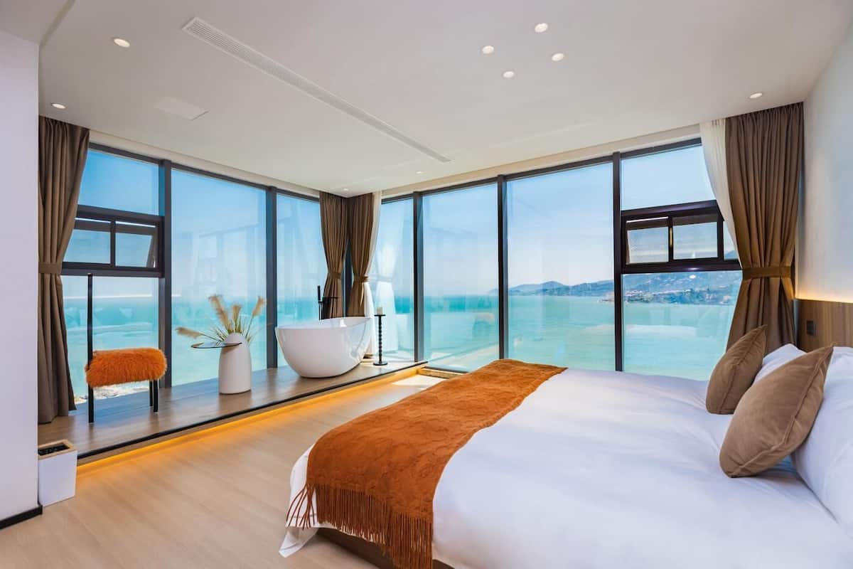 Habitación de hotel moderna con una cama grande, una bañera y vista al mar.