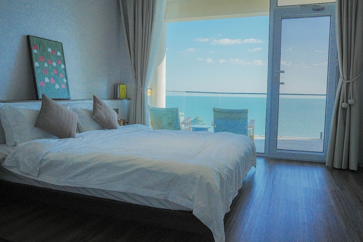 Habitación de hotel con una cama grande, un balcón con vistas y un cuadro en la pared.