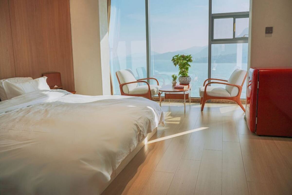 Una habitación de hotel moderna con una cama grande, dos sillones, una mesita con una planta y un armario rojo.