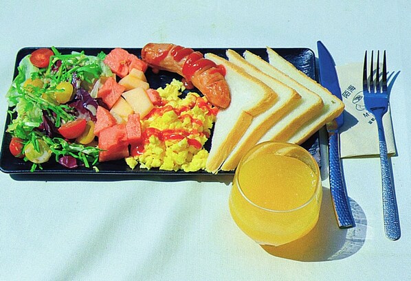 A meal consisting of scrambled eggs, sausage, toast, a salad, and a glass of orange juice on a black plate.