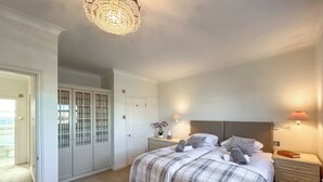 Ein Schlafzimmer mit einem Bett, Nachttischen, einem Schrank und einer Tür, die in einen anderen Raum führt, sowie einer Deckenleuchte.