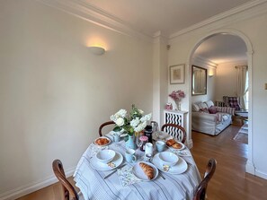 A dining area with a table set for two, a sofa in the background, and a mirror above the sofa.