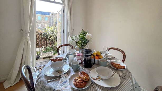 Ein Esstisch ist gedeckt mit Tellern, Schüsseln, einer Blumenvase und einem Croissant.
