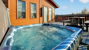 Una cabaña de madera con jacuzzi, terraza y un porche cubierto con mesas.
