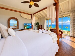 Ein Hotelzimmer mit einem großen Bett, einem Deckenventilator, einem Fernseher und Blick auf den Ozean.