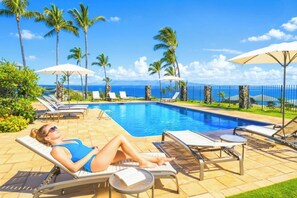 Un espace aménagé au bord de la piscine, avec des chaises longues, des parasols et une vue sur l’océan.