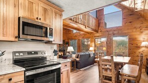 Interior de una cabaña de madera con cocina, comedor y un dormitorio en el altillo.