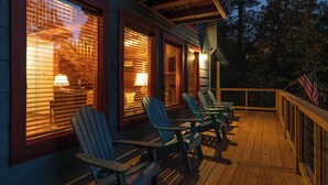 Una terraza de madera con sillas Adirondack y barandilla, con vistas a un área boscosa.