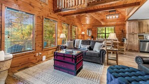 Interior acogedor de una cabaña con detalles de madera, un sofá, una mesa de comedor y una zona de cocina.