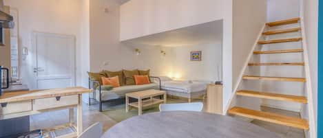A compact living space with a sofa, a dining table, a staircase, and a kitchen area.