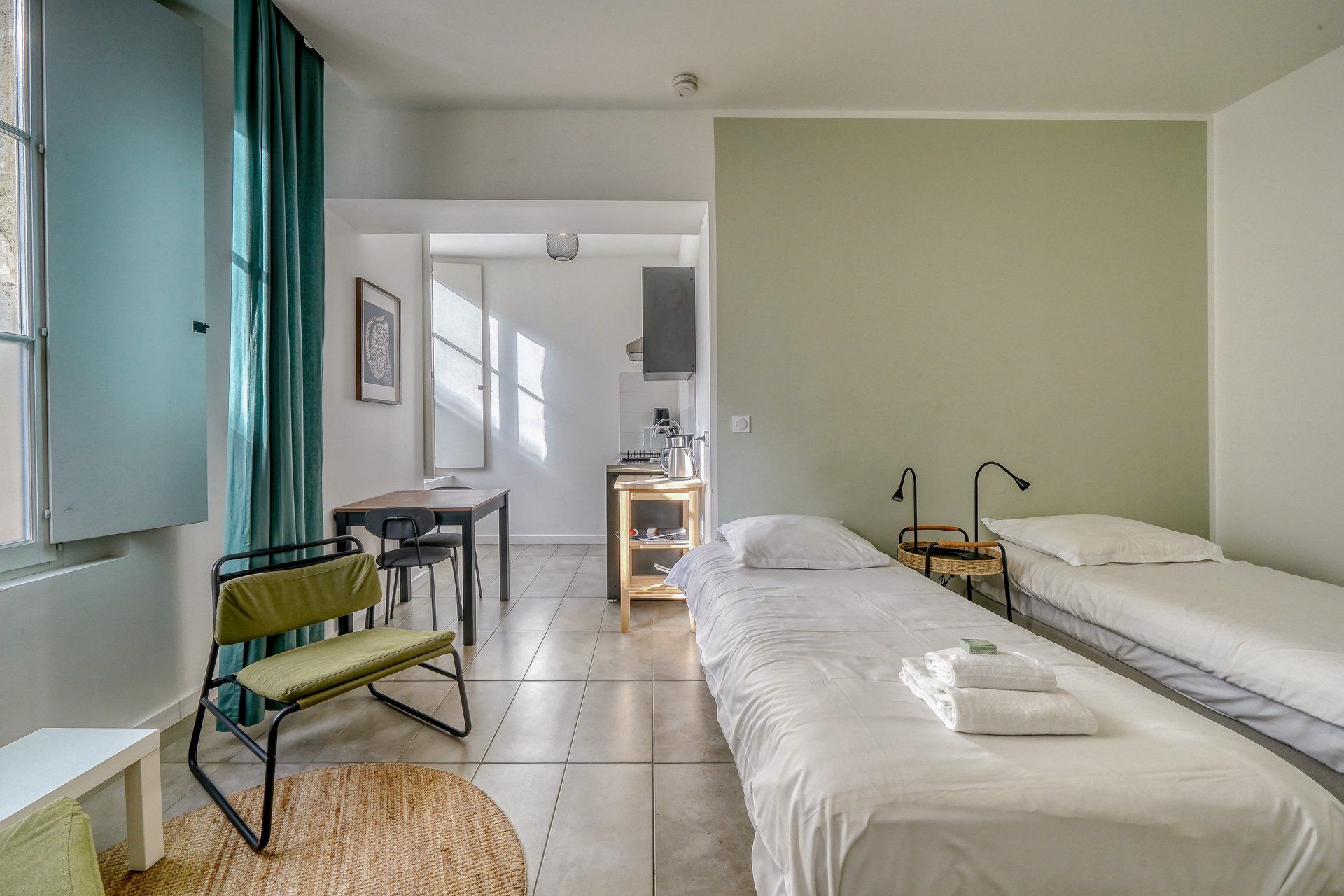 A hotel room with a bed, a desk, a chair, a small table, and a window with curtains.