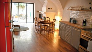 Una cocina con piso de madera, una mesa de comedor con sillas, una puerta roja y vistas al exterior por una puerta corredera.