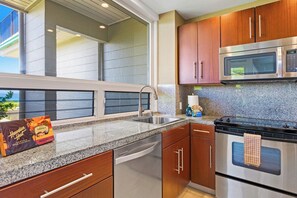 A modern kitchen with granite countertops, stainless steel appliances, and wooden cabinets. - Kapalua Bay | Ocean View 2 BR, Sleeps 6 | Car Incl. w/ 6+ Nights | KBV ML-1984 by KBM (Lahaina)