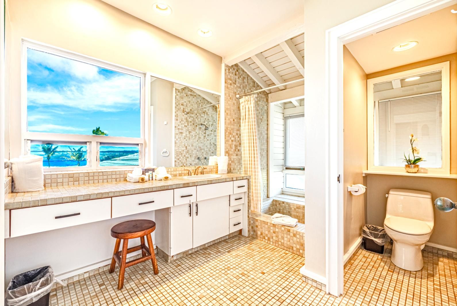 A bathroom with a large window, a shower, a toilet, and a sink with a mirror.