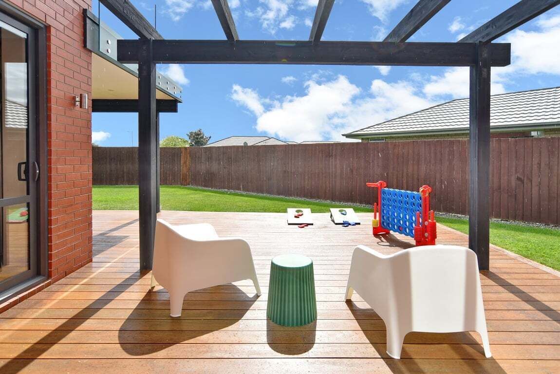 Eine Terrasse im Freien mit Holzdeck, zwei weiße Plastikstühle, ein grüner Hocker und ein Tisch.