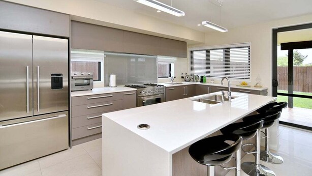 Una cocina moderna con electrodomésticos de acero inoxidable, una isla central con taburetes y un amplio ventanal que proporciona luz natural.