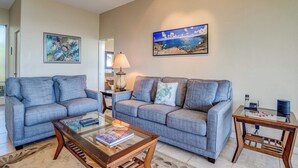 A living room with two grey sofas, a glass coffee table, a lamp, and a painting of a beach scene. - Kapalua Bay | Ocean View 3 BR, Sleeps 10 | Car Incl. w/ 6+ Nights | KBV ML-1969 by KBM (Lahaina)