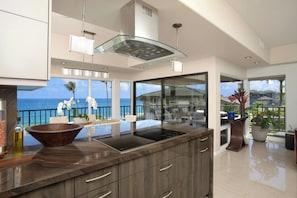 A modern kitchen with a large island, a glass-enclosed dining area, and a view of the ocean. - Kapalua Bay | Ocean View 3 BR, Sleeps 8 | Car Incl. w/ 6+ Nights | KBV ML-1993 by KBM (Lahaina)