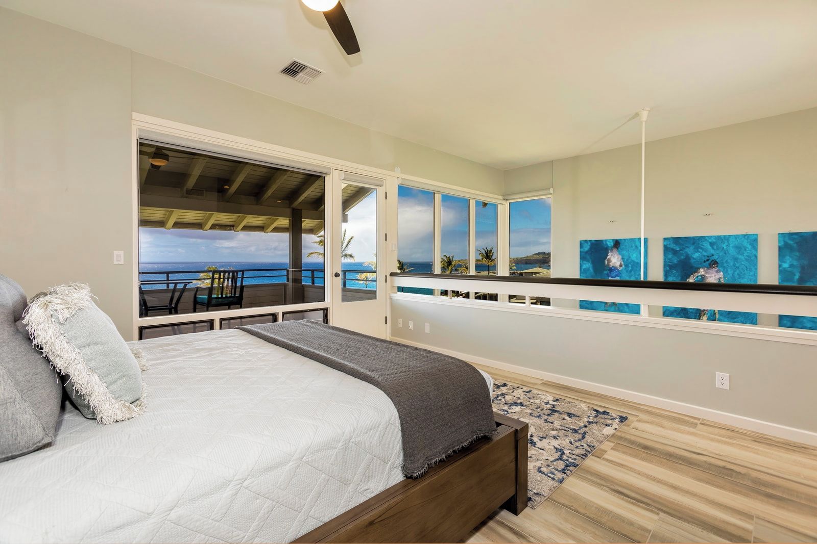 A bedroom with a bed, a view of the ocean, and artwork on the wall.
