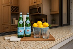A kitchen counter with two Pellegrino water bottles, a bowl of lemons, and three glasses. - Kapalua Bay | Ocean View 3 BR, Sleeps 10 | Car Incl. w/ 6+ Nights | KBV ML-1987 by KBM (Lahaina)