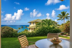A two-story house with a view of the ocean, a lawn, and a table with chairs and a bowl of fruit. - Kapalua Bay | Ocean View 3 BR, Sleeps 10 | Car Incl. w/ 6+ Nights | KBV ML-1987 by KBM (Lahaina)