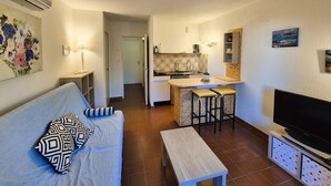 A compact living space with a kitchenette, a sofa with patterned cushions, a television, and artwork on the walls. - Ground-floor studio, air conditioning, close to the sea, parking (ST MANDRIER SUR MER)