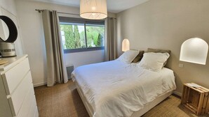 Ein Schlafzimmer mit einem Bett, einem Schminktisch, einem Spiegel, einem Fenster mit Vorhängen und einer Wandleuchte.
