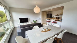 Ein moderner Wohnraum mit Essbereich, Sofa, Fernseher und einer Küche im Hintergrund.