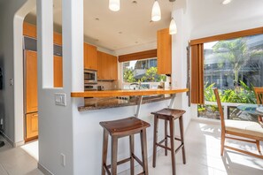 A modern kitchen with wooden cabinets, a built-in oven, and a bar area with stools. - Kapalua Bay | Ocean View 2 BR, Sleeps 6 | Car Incl. w/ 6+ Nights | KBV ML-2011 by KBM (Lahaina)