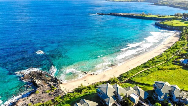 An aerial view of a coastal resort with a beach, clear blue waters, and modern buildings. - Kapalua Bay | Ocean View 2 BR, Sleeps 8 | Car Incl. w/ 6+ Nights | KBV ML-1996 by KBM (Lahaina)