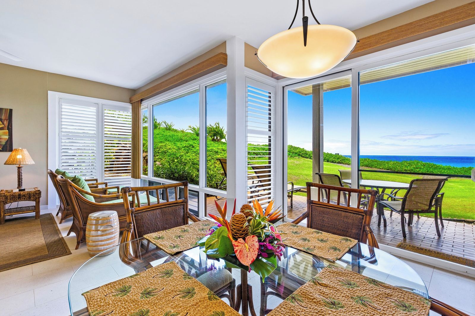 A dining area with a glass table, wicker chairs, and a view of the ocean.